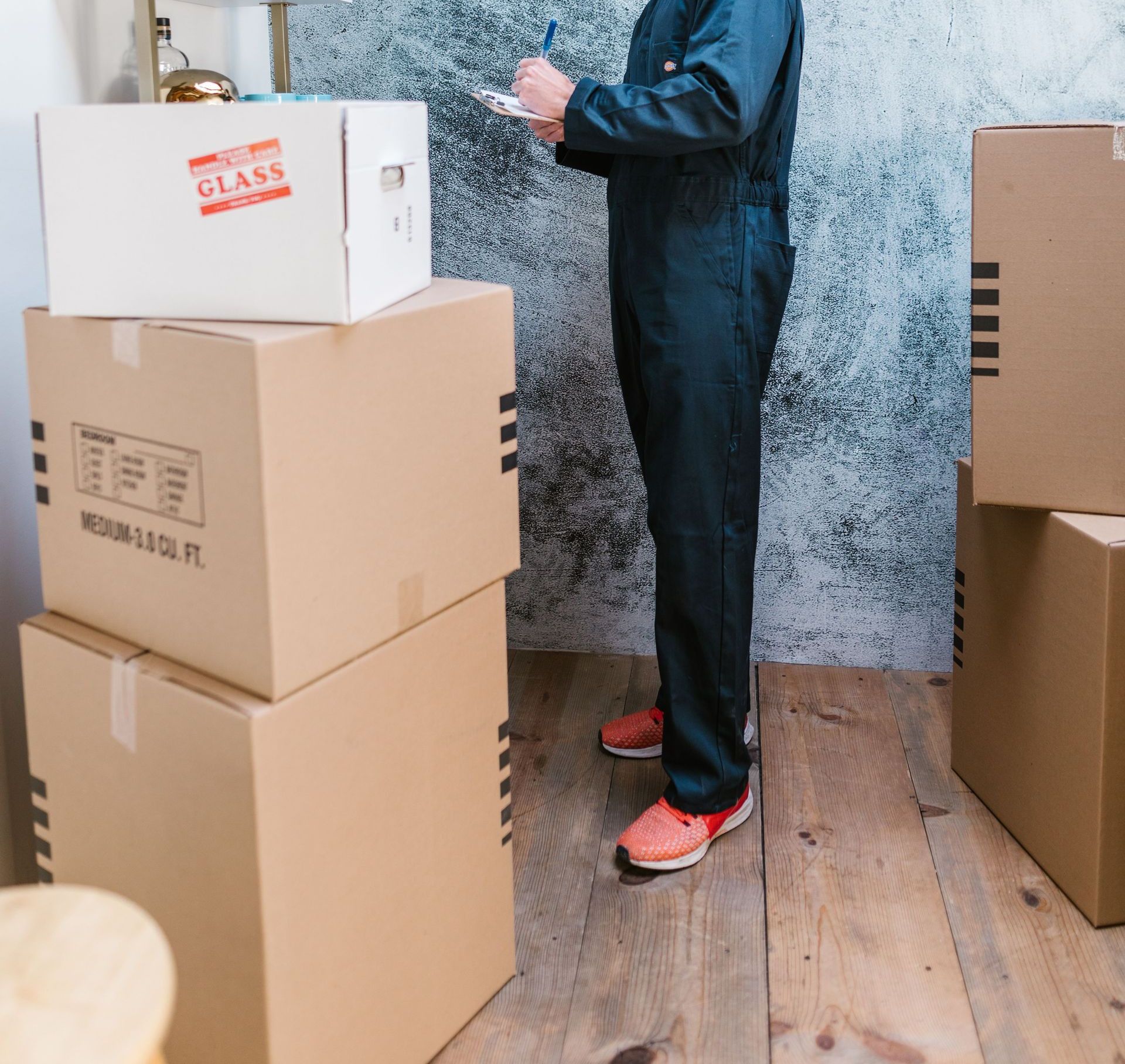 A Caucasian mover in coveralls packing and organizing cardboard boxes indoors.
