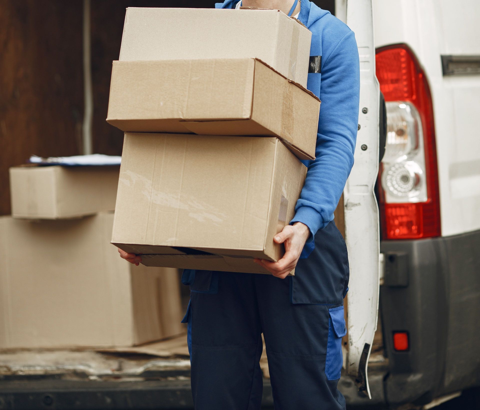 Man wearing mask delivering cardboard boxes from van outdoors.