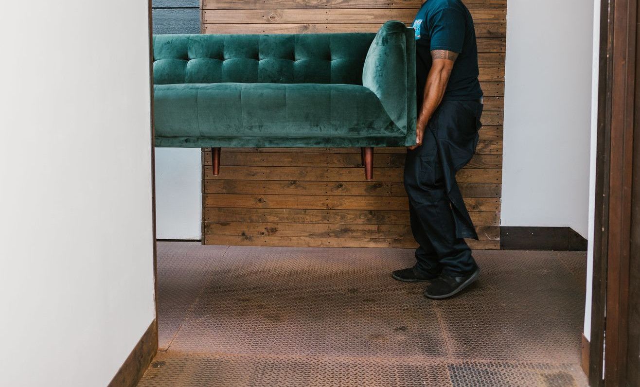 A mover carries a green sofa indoors, showcasing modern interior design and relocation services.