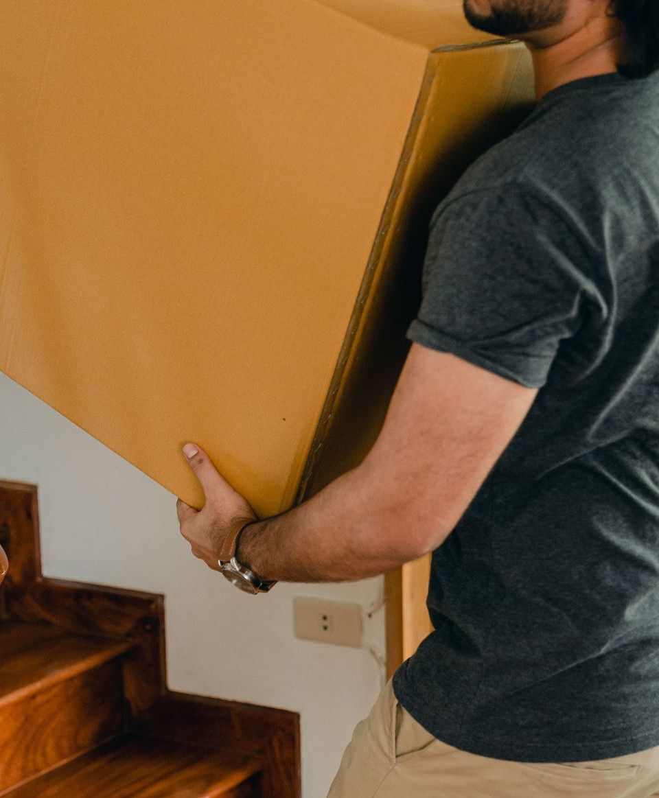 Crop unrecognizable couple carrying personal items in big carton box down stairs while moving to new apartment